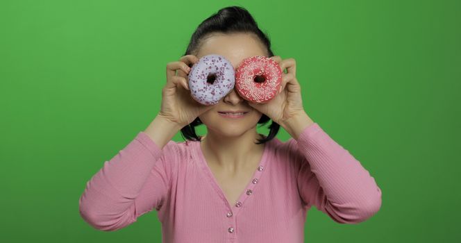 Happy beautiful young girl on a chroma key background having fun with donuts. Cute woman in a pink shirt posing with donuts. Making faces