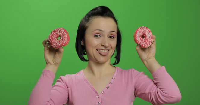 Happy beautiful young girl on a chroma key background having fun with donuts. Cute woman in a pink shirt posing with donuts. Making faces