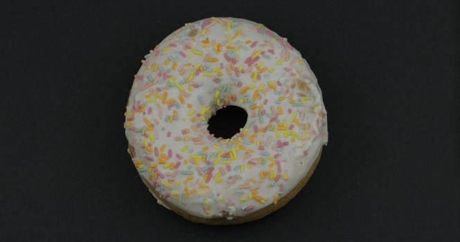 Delicious, tasty and fresh donut. Top view. Bright and colorful sprinkled sweet white donut close-up macro shot on a black background