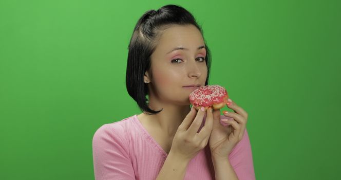 Happy beautiful young girl on a chroma key background wants to eat a donut. Cute woman in a pink shirt posing with donut