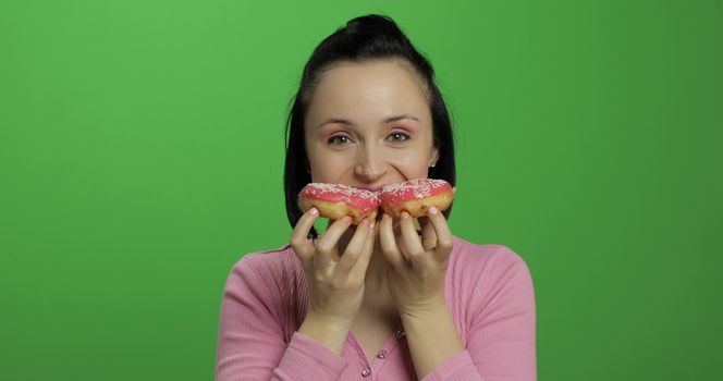 Happy beautiful young girl on a chroma key background having fun with donuts. Cute woman in a pink shirt posing with donuts. Making faces