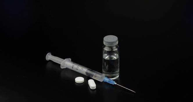 Pills, syringe and ampoule with vaccination on black background.