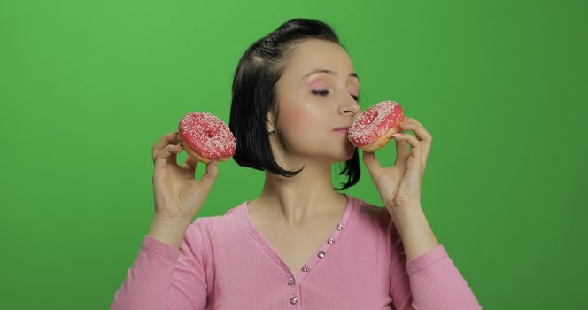 Happy beautiful young girl on a chroma key background having fun with donuts. Cute woman in a pink shirt posing with donuts. Making faces