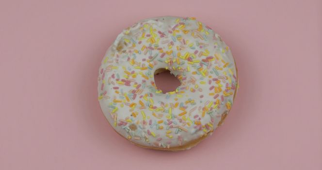 Delicious, tasty and fresh donut. Top view. Bright and colorful sprinkled white sweet donut close-up macro shot on a pink background