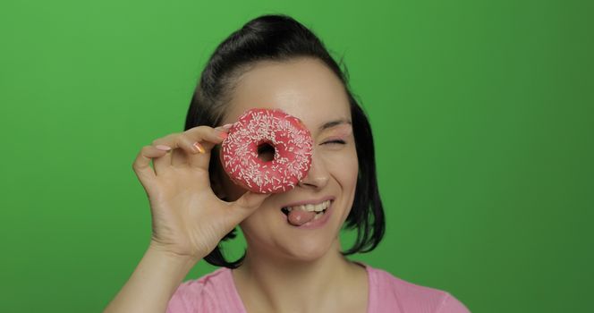 Happy beautiful young girl on a chroma key background having fun with donuts. Cute woman in a pink shirt posing with donuts. Making faces