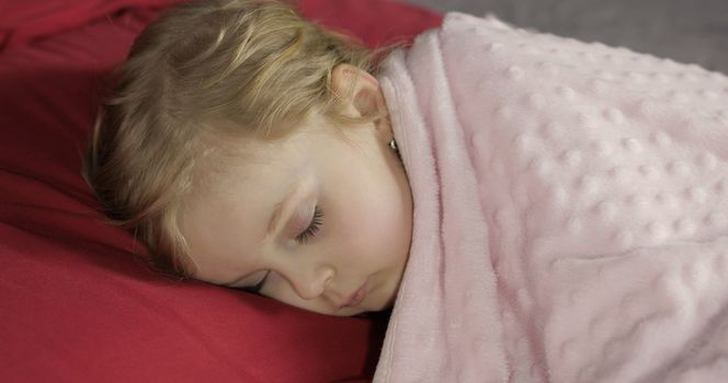 Cute baby girl sleeping on cozy bed at home. Pretty, little girl sleeping in morning light. Close-up portrait of child naps. Concept of peaceful sweet dreams