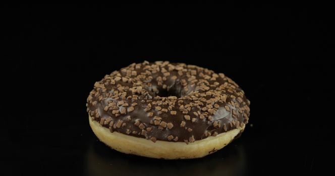 Delicious, tasty and fresh donut. Bright and colorful sprinkled sweet brown donut close-up macro shot on a black background