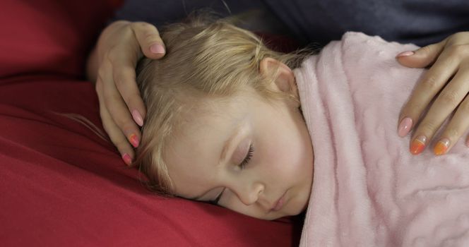 Young mother taking care of her little baby girl while she sleep. Girl sleeping on cozy bed at home. Pretty girl sleeping in morning light. Close-up portrait of child naps. Concept of peaceful dreams