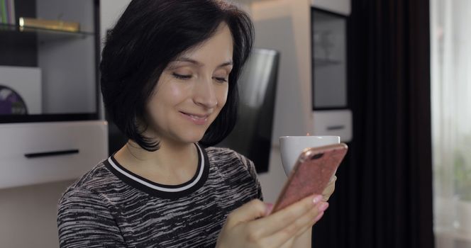 Portrait of pretty caucasian young brunette woman having chat on social media using smartphone enjoying chatting to friend. At home