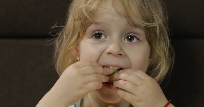 Beautiful little blonde girl sitting on a sofa at home and eating corn puffs. Cute child taste puffcorns. Inside. Childrens meal