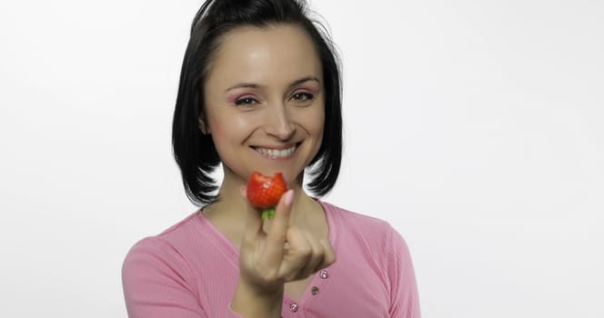 Young beautiful woman with fresh and juicy strawberry offer bite to viewer. Healthy nutrition