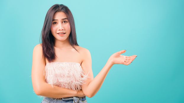 Smiling face Asian beautiful woman her showing hand something near body on blue background, with copy space for text