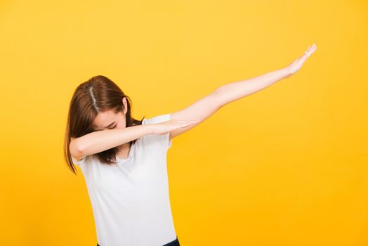 Asian happy portrait beautiful cute young woman teen smile standing wear t-shirt move showing DAB dance against gesture isolated, studio shot on yellow background with copy space