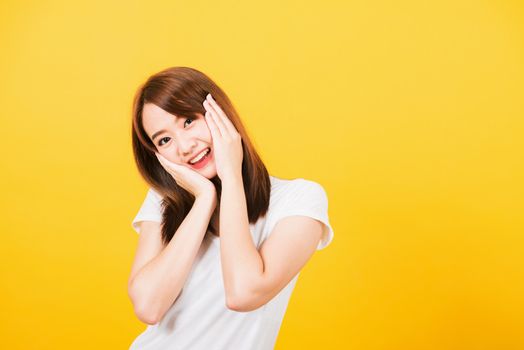 Asian happy portrait beautiful cute young woman teen stand surprised excited celebrating open mouth gesturing palms on face looking to camera isolated, studio shot yellow background with copy space