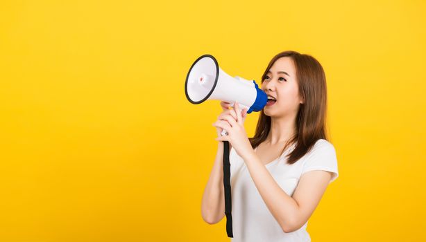 Asian happy portrait beautiful cute young woman teen standing making announcement message shouting screaming in megaphone looking to side isolated, studio shot on yellow background with copy space