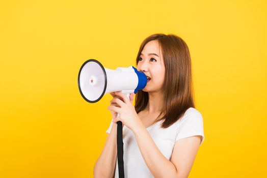 Asian happy portrait beautiful cute young woman teen standing making announcement message shouting screaming in megaphone looking to side isolated, studio shot on yellow background with copy space