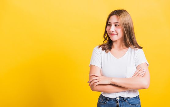 Asian Thai happy portrait beautiful cute young woman standing wear t-shirt her smile confidence with crossed arms looking to side up isolated, studio shot on yellow background and copy space