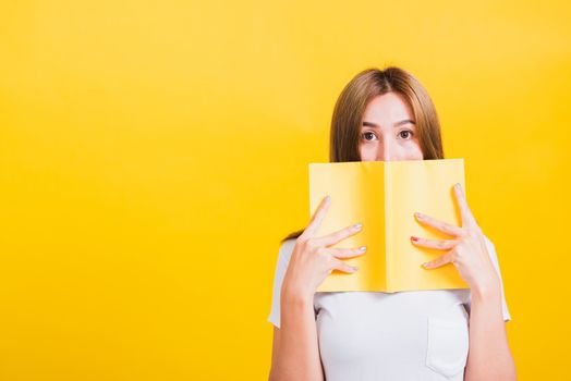 Portrait Asian Thai beautiful happy young lifestyle woman stands holding yellow book or diary her looking to camera, studio shot isolated on yellow background, with copy space