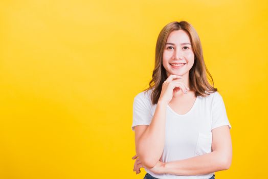 Portrait Asian Thai beautiful young woman wearing white t-shirt standing chin handle relaxed thinking about something about the question studio shot, isolated on yellow background with copy space