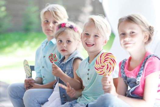 Four funny kids cute smiling friends eat enjoy lollipops outdoors