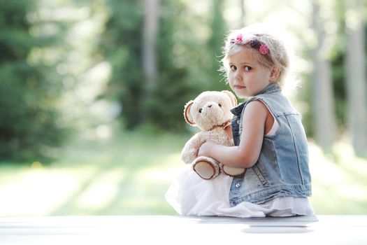 Worried Little girl holding her Teddy bear sitting outdoors