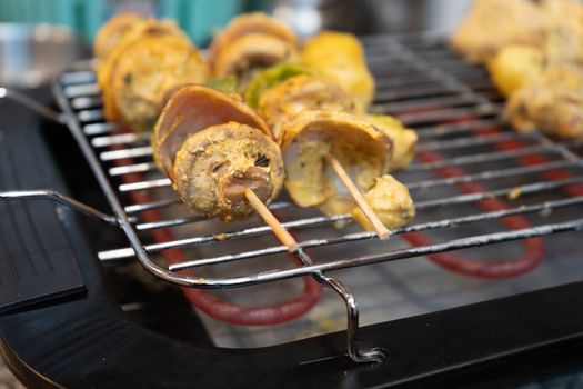 Wooden skewer with vegetables like mushroom, chilli pepper, green pepper onions and potatoes cooking on an electric grill . Tasty home barbeque for a healthy non fried snack or meal