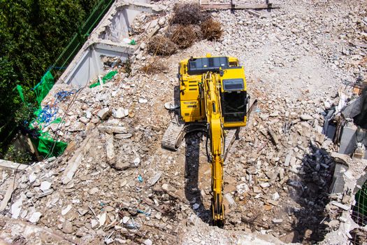 The backhoe machinery working on site demolition of an old building workers spray water to get rid of dust.