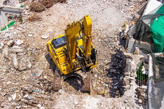 The backhoe machinery working on site demolition of an old building workers spray water to get rid of dust.