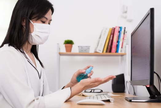 A beautiful Asian businesswoman wearing a mask does cleaning hands with cleaner gel to protect COVID-19 before start working from home with safety and happiness.