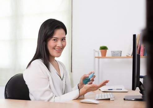 A beautiful Asian businesswoman cleaning hands by cleaner gel to protect COVID-19 before start working from home with safety and happiness.