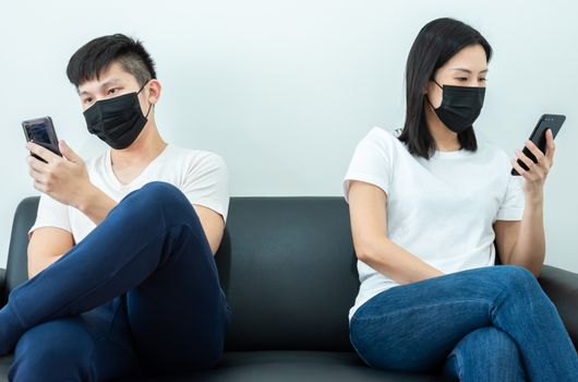 An Asian couple stays together and playing the phone with black mask and social distancing.