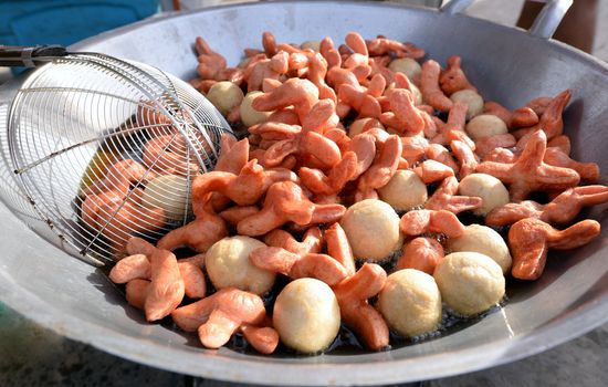 Meatballs and Sausages frying in a large pan with boiling oil