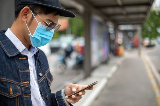 Asian Young man using smart phone in the city and wearing face mask for protection air pollution, particulates and for protection flu virus, influenza, coronavirus