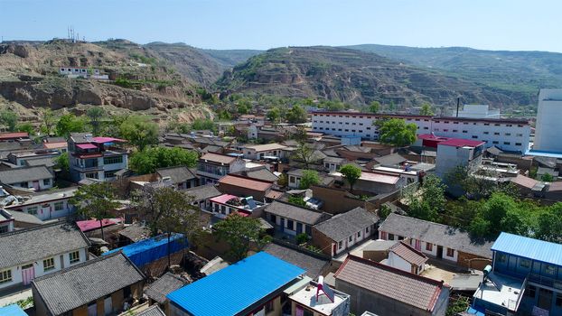 Aerial view of small poor town next the arid terraced farm firld mountain in Gansu region, China