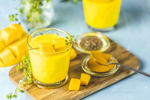 Yellow Indian mango yogurt drink Mango Lassi or smoothie with turmeric and saffron. Healthy probiotic Indian cold summer drink on blue background.