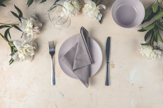 Flat lay composition with white peony flowers, empty plate with napkin and cutlery  on a light pink concrete background