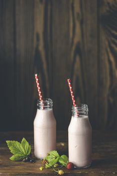 Bottles with delicious strawberry milkshake or smoothie with branch of wild strawberry on dark wooden table and background.