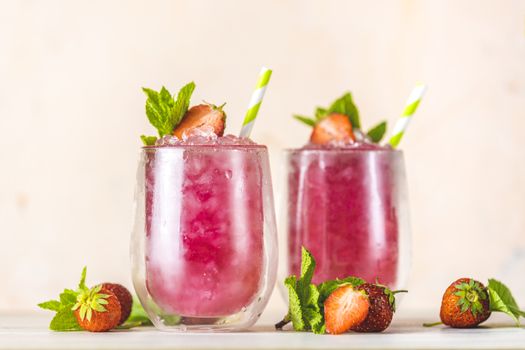 Fresh strawberry cocktail. Fresh summer cocktail with strawberry and ice cubes. Glass of strawberry soda drink on light pink background.