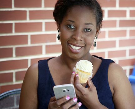 African American women holding cupcake and phone on brick wall background