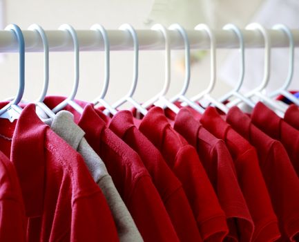 Red and one gray school uniform shirts on hangers. Selective focus.