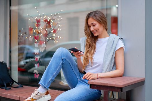 Woman city street summer sitting bench smartphone showcase shop window outdoor Modern stylish travel girl with backpack resting happy smiling Middle age female alone chatting mobile cell phone