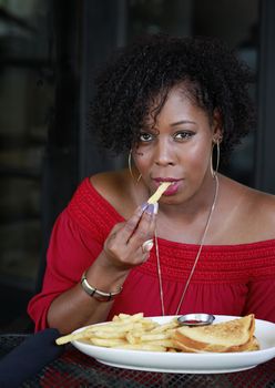 Beautiful African American woman with fancy manicure enjoying Sandwich and french fries