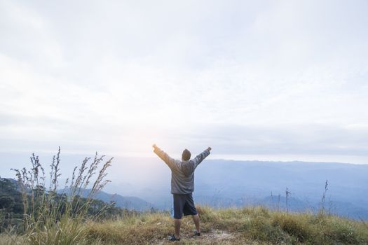 Happy young man standing with raised arms in mountains