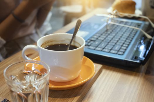 Cup of coffee and laptop on wooden table in coffee shop