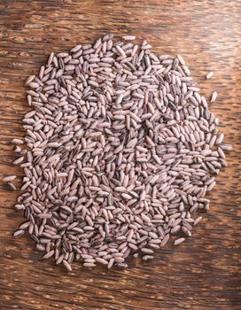 Red rice on a dark wooden plate, top view, vertical.