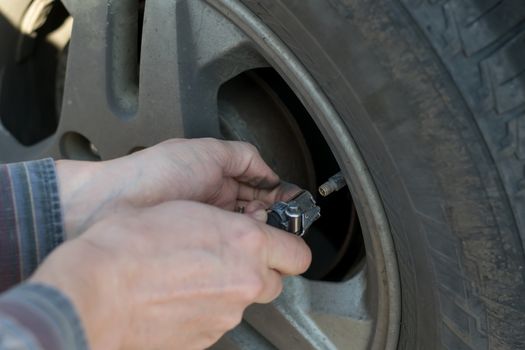 human hands insert the hose of the car pump to pump air into the wheel of the car