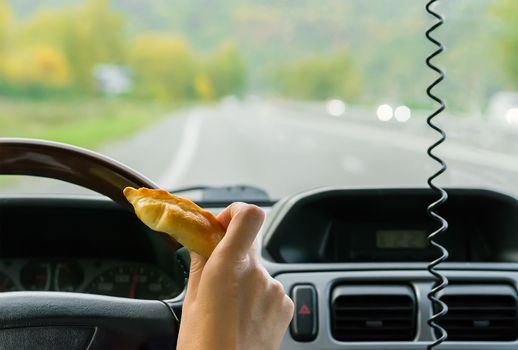 Closeup, of female hand holding a bun behind the wheel of the car in motion on highway