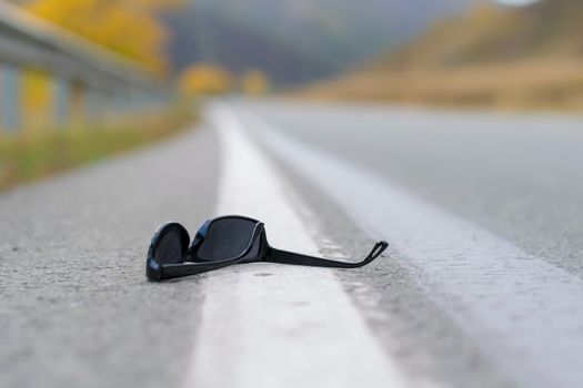 close up, lost sunglasses lie on the road asphalt on a country track on the dividing strip at the curb