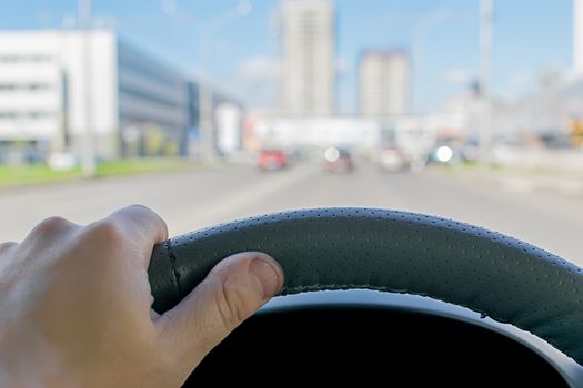 the driver's hand on the steering wheel of a car that passes on the highway against the background of city buildings and office centers