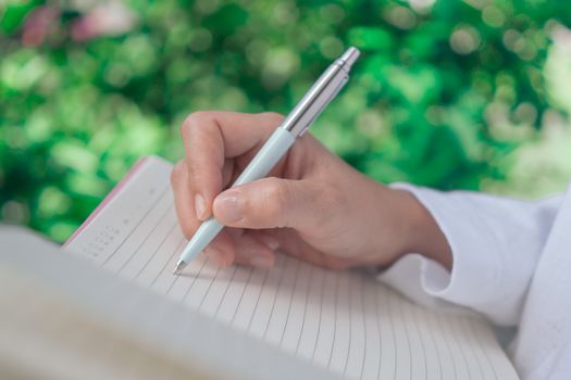 Woman hand writing down in small white memo notebook for take a note not to forget or to do list plan for future.